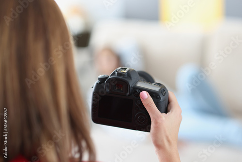 Woman holds professional black camera in hands and photographs model at home photo