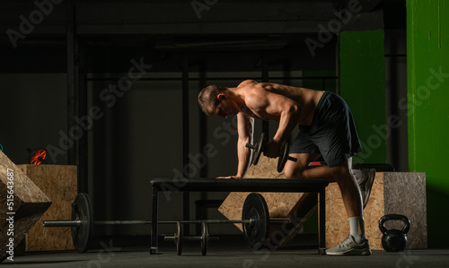 Good looking young man doing triceps dumbbell kickback exercises with his left hand photo