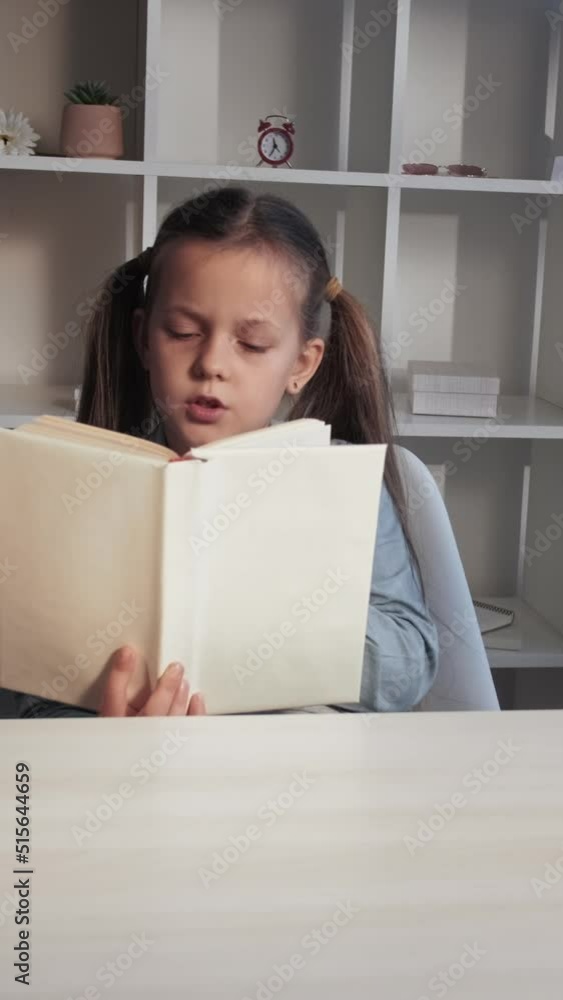 Vertical video. Kid reading. Children education. Home learning. Motivated intelligent little girl studying with open book at workplace. Vertical video. Kid reading. Children education. Home learning. Motivated intelligent little girl studying with open book at workplace.