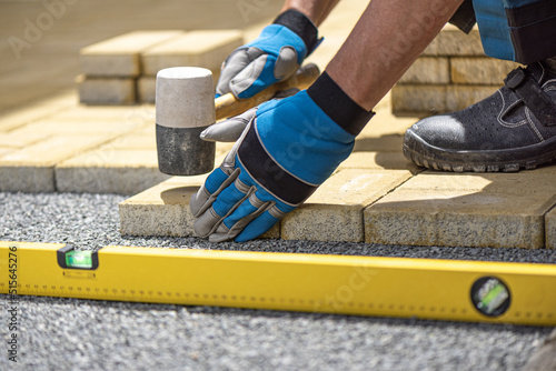 The hand of the worker using a rubber hammer and water-level for aligns the interlocking paving stone. photo