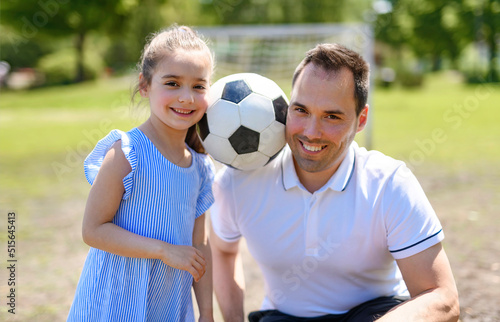 Young father with his little daughter playing football on football pitch