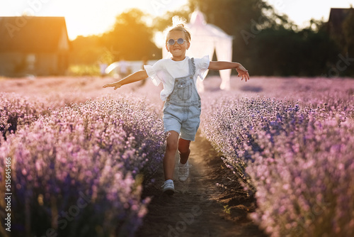 Wallpaper Mural happy child girl is walking in lavender field on sunset. Smiling kid in suglasses , jeans jumpsuit is having fun in nature on summer day. Cheerful little girl. happy childhood concept Torontodigital.ca