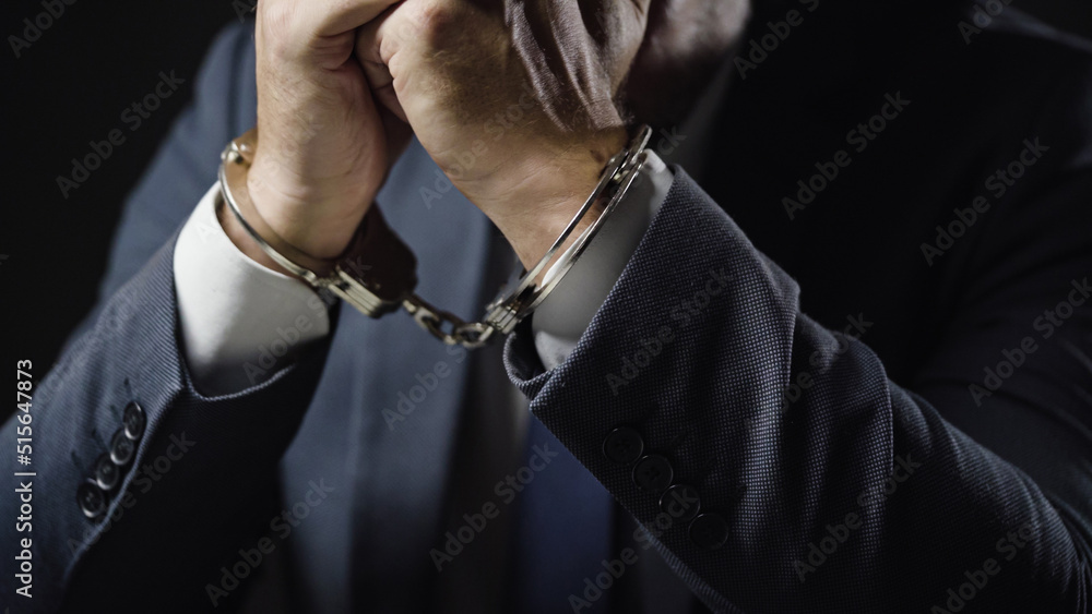 Businessman in handcuffs arrested for financial fraud, sitting in interrogation room