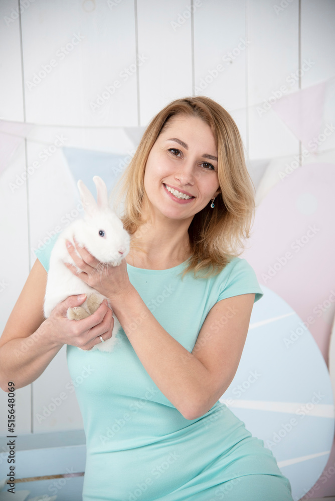smiling beautiful blond woman in blue dress playing with white rabbit in white studio. easter smiling beautiful blond woman in blue dress playing with white rabbit in white studio. easter
