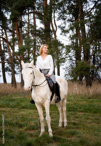 smiling blonde beautiful woman riding  white blue eyed  horse horse in green forest  © Tetatet