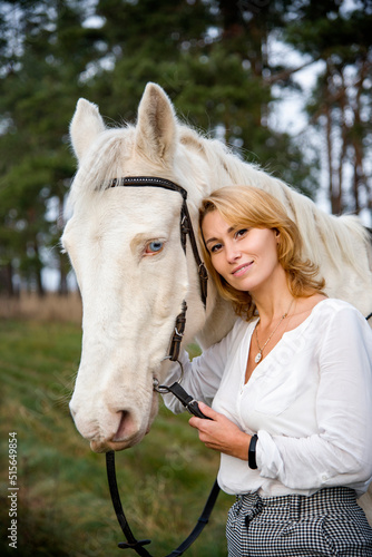 smiling blonde beautiful girl walking with white blue eyed  horse horse in green forest  © Tetatet