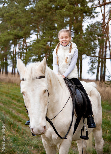 Cute girl sitting on a white blue eyed horse in the autumn forest 
