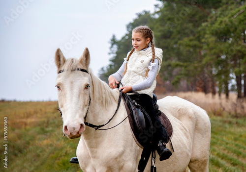 Cute girl sitting on a white blue eyed horse in the autumn forest 