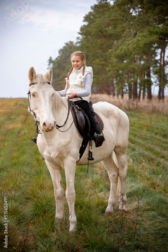 Cute girl sitting on a white blue eyed horse in the autumn forest  © Tetatet
