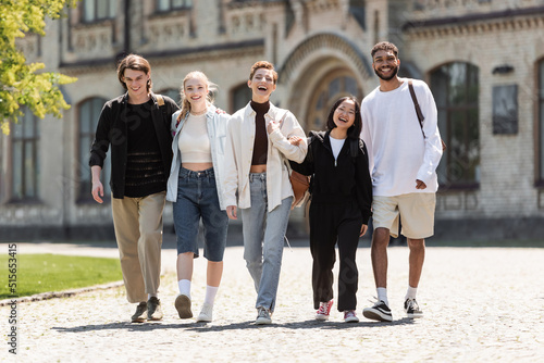 Young multiethnic students walking and looking at camera near university outdoors.