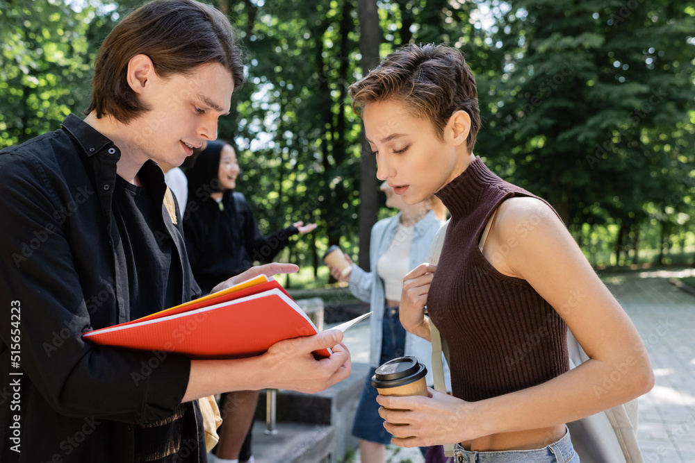 Students with coffee to go looking at notebook in park. Students with coffee to go looking at notebook in park.