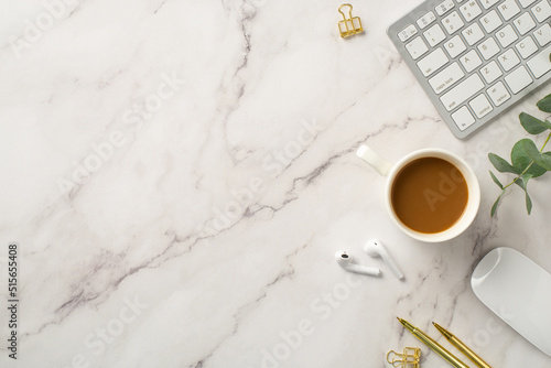 Business concept. Top view photo of workstation keyboard computer mouse cup of coffee wireless earbuds gold pens binder clips and eucalyptus on white marble background with blank space photo