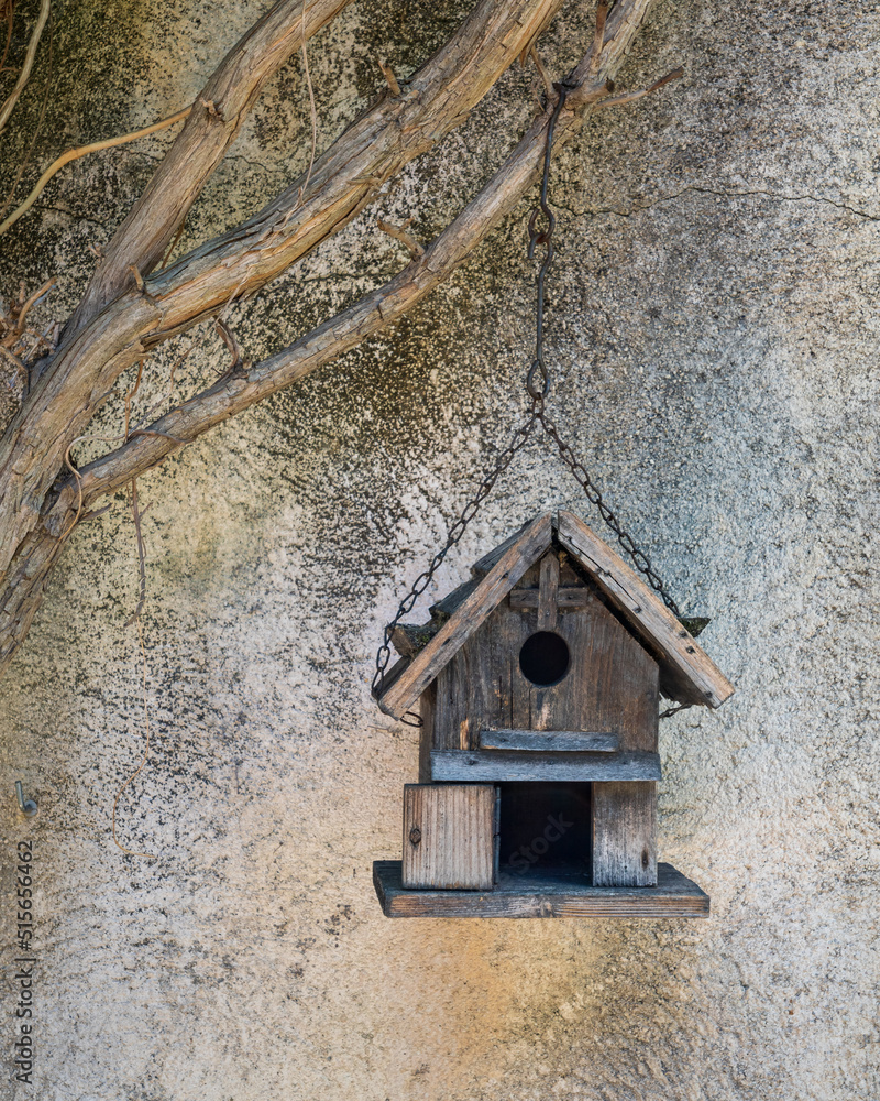 Small and cute traditional handmade wooden birdhouse hanging outdoors on chain against garden wall