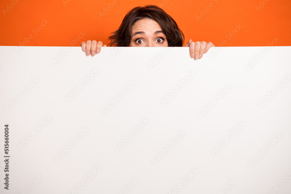 Portrait of puzzled person eye peeking behind empty space blank isolated on orange color background Portrait of puzzled person eye peeking behind empty space blank isolated on orange color background