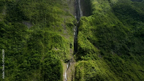 Aerial view of a waterfall on the side of a mountain on the Reunion Island. Sunlight break through the clouds, the mountain is covered in green vegetation.