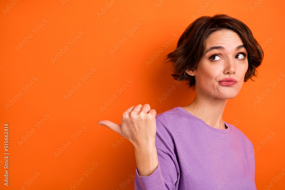 Photo of funky unsure lady wear violet sweatshirt looking pointing thumb back empty space isolated orange color background Photo of funky unsure lady wear violet sweatshirt looking pointing thumb back empty space isolated orange color background