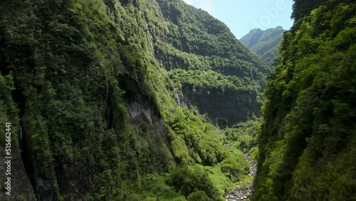 Aerial view of a tropical ravine at noon in the Reunion Island. There is a river at the bottom of the ravine. There is green vegetation on both sides of the ravine. 4k footage photo