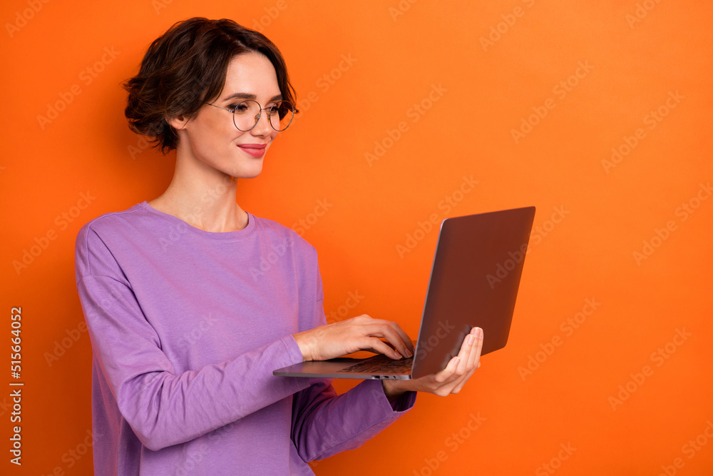 Portrait of smart positive lady hold use wireless netbook write email isolated on orange color background Portrait of smart positive lady hold use wireless netbook write email isolated on orange color background