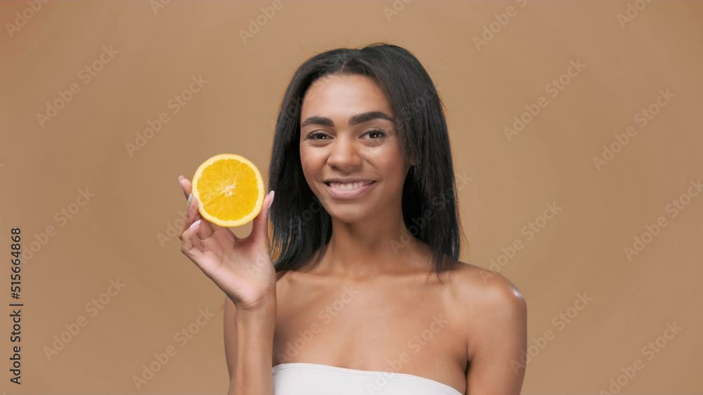 Smily attractive African american girl having two pieces of orange, enjoying smell freshness with smile looking at camera over the pastel background Smily attractive African american girl having two pieces of orange, enjoying smell freshness with smile looking at camera over the pastel background