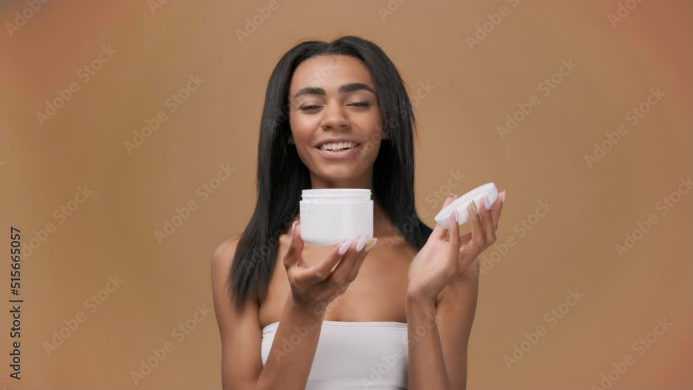 Happy smily attractive African American girl holding face cream jar.Skincare cosmetics, routine beauty treatment. Happy smily attractive African American girl holding face cream jar.Skincare cosmetics, routine beauty treatment.
