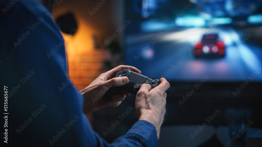 Close Up on Man's Hands at Home, Sitting on a Couch in Stylish Loft Apartment and Playing Arcade Car Video Games on Console. Male Using Controller to Play Street Racing Drift Simulator.