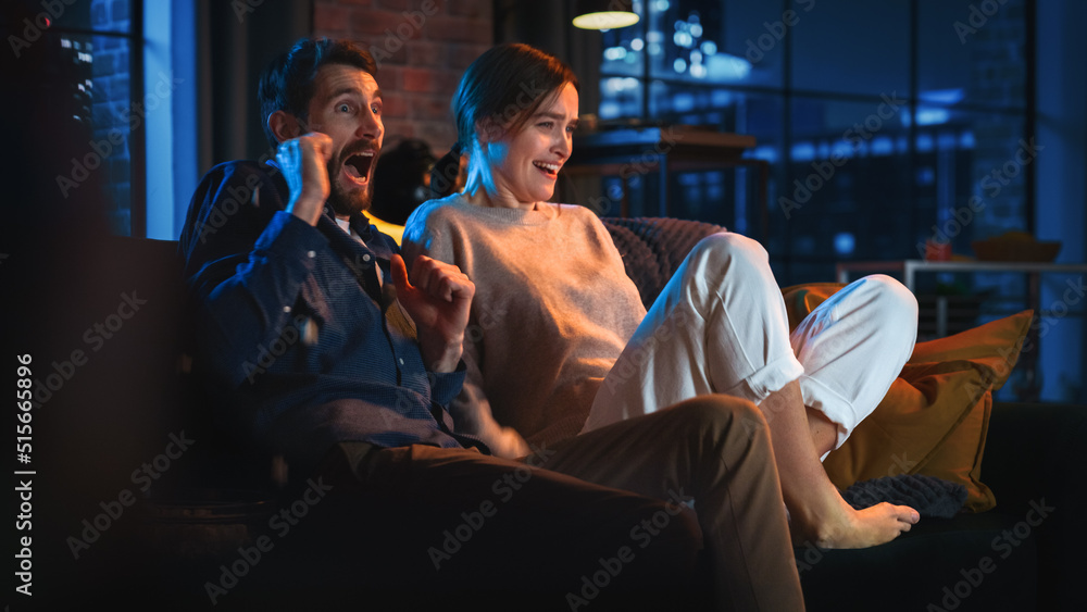 Obraz premium Portrait of Beautiful Couple Spending Time at Home, Sitting on a Couch, Watching Scary TV Show in Their Stylish Loft Apartment. Man and Woman Streaming Horror Movie and Get Scared and Surprised.