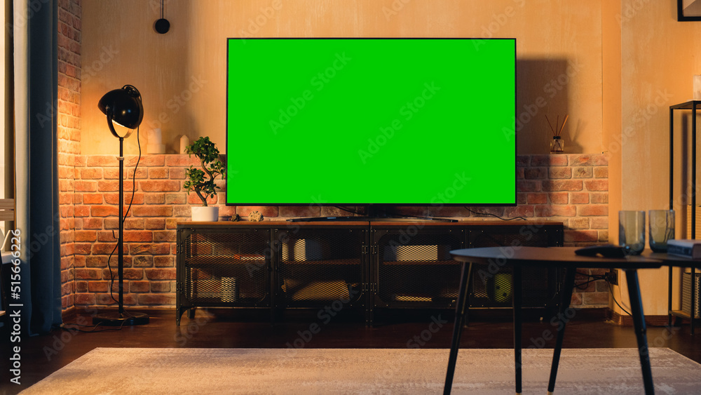 Foto Stock Stylish Loft Apartment Interior with TV Set with Green Screen  Mock Up Display Standing on Television Stand. Empty Living Room at Home  with Chroma Key Placeholder on Monitor. Sunset Warm