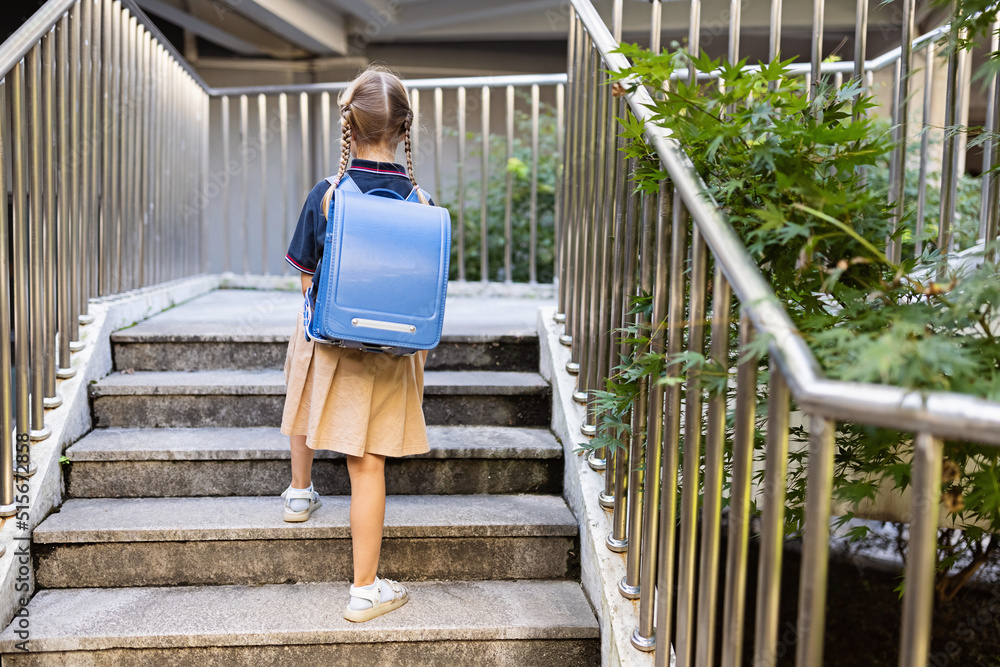 Schoolgirl back to school after summer vacations. Child in uniform standing early morning outdoor. Lifestyle portrait of Little caucasian girl with blonde hair six-seven years old from elementary