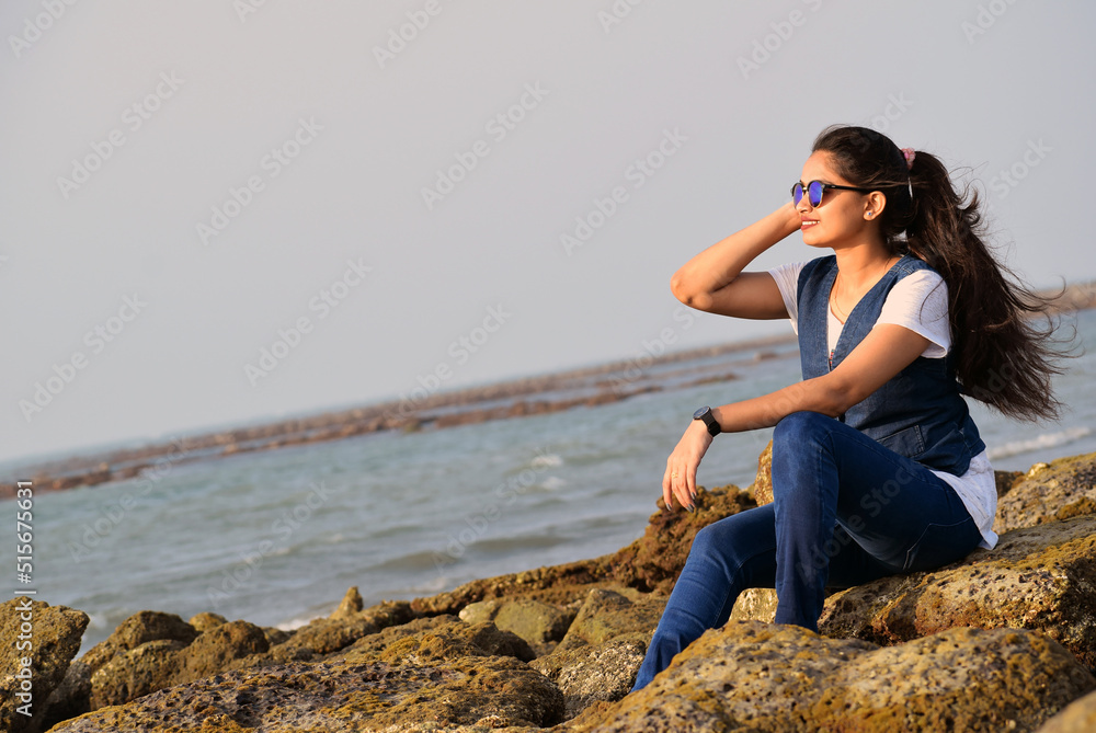 Beautiful young lady enjoying the sea beach wearing sunglass. Young girl wearing jeans and tops with a big smile on face looking at the sea