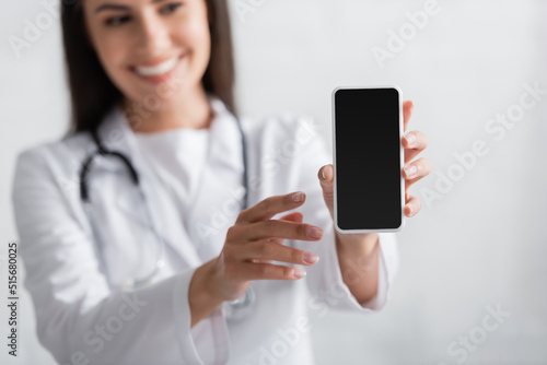 Blurred brunette doctor holding smartphone with blank screen