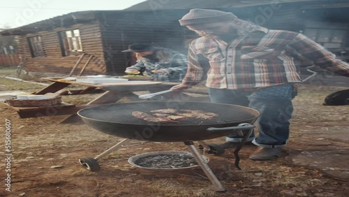 Vertical format footage of man taking off lid frim bbq grill and turning meat with metal tongues while cooking food outdoors photo