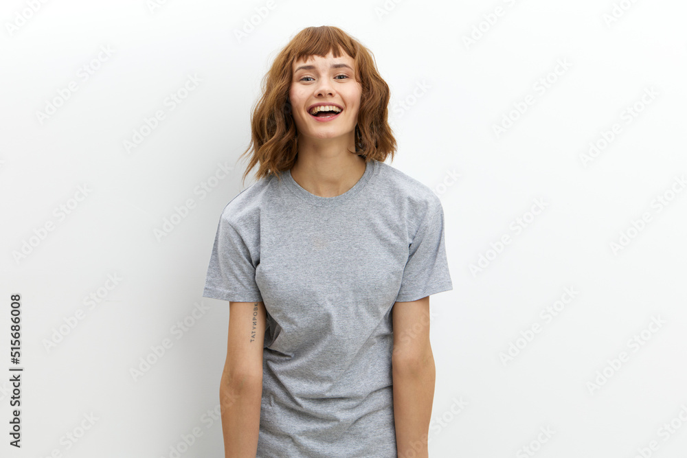 a happy, joyful woman in a gray cotton T-shirt stands against a light background, smiling happily and looking at the camera. Horizontal photo with an empty space for inserting an advertising layout a happy, joyful woman in a gray cotton T-shirt stands against a light background, smiling happily and looking at the camera. Horizontal photo with an empty space for inserting an advertising layout