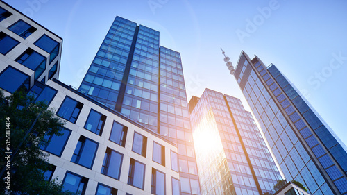 Bottom view of modern skyscraper in business district against blue sky. Looking up at business buildings in downtown. Rising sun on the horizon.