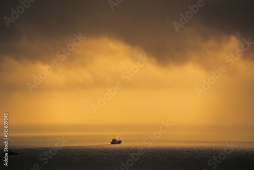 Silhouette of a ship cruising on a calm coast during sunset photo