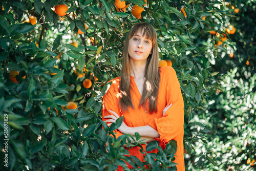 Pretty girl in orange dress is posing to camera by crossing arms in orange garden