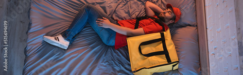 Top view of young somnambulist in delivery uniform sleeping near thermo backpack on bed, banner