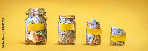 Four glass jars with yellow blank stickers, savings, cash money (euro banknotes) on yellow background