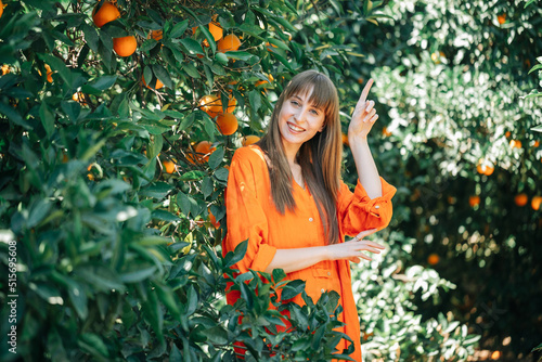 Happy young girl is pointing up with forefinger in orange garden