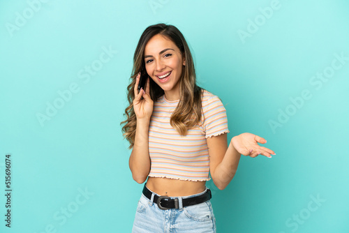 Young woman over isolated blue background keeping a conversation with the mobile phone with someone