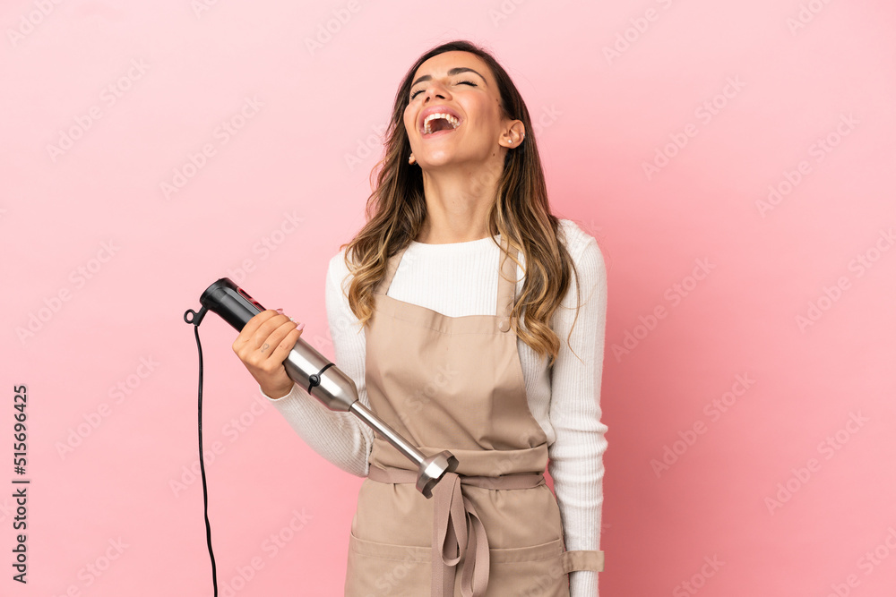 Young woman using hand blender over isolated pink background laughing Young woman using hand blender over isolated pink background laughing