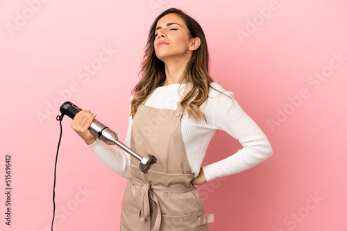 Young woman using hand blender over isolated pink background suffering from backache for having made an effort