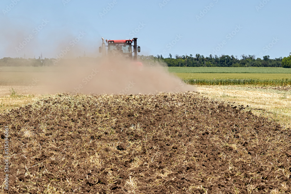 Fototapeta premium Plowed land in the field, against the backdrop of a working tractor