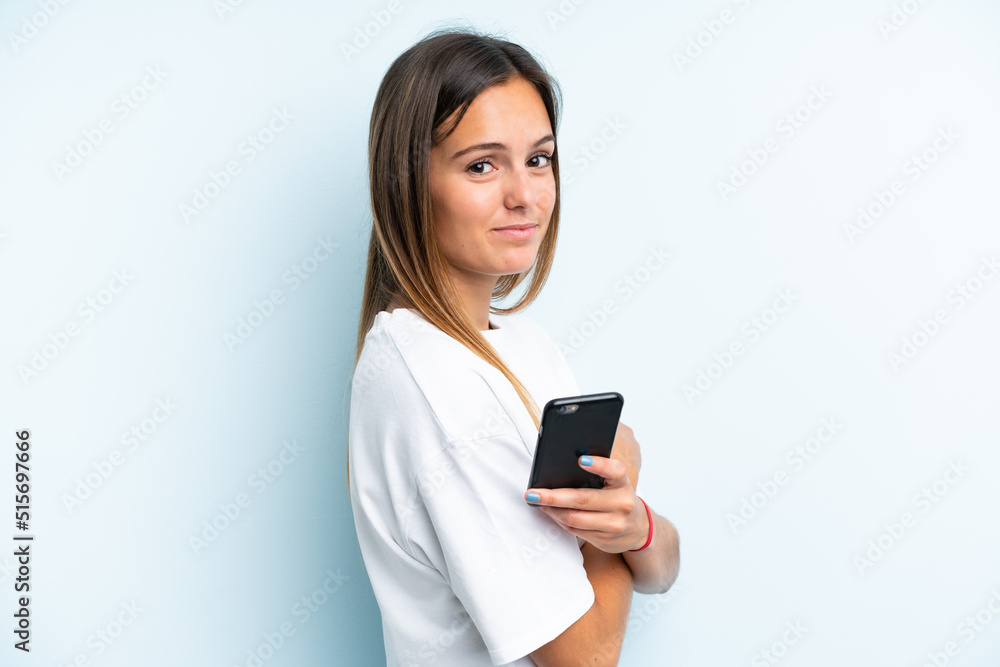 Young caucasian woman isolated on blue background holding a mobile phone and with arms crossed Young caucasian woman isolated on blue background holding a mobile phone and with arms crossed