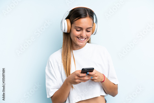 Young caucasian woman isolated on blue background listening music and looking to mobile