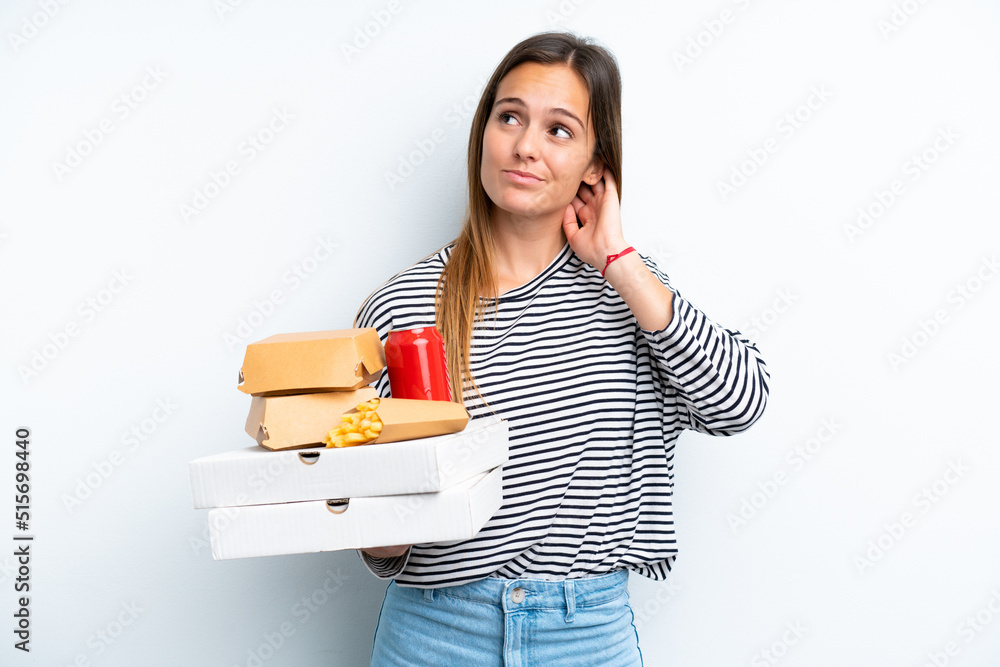 Young caucasian woman holding fast food isolated on white background having doubts Young caucasian woman holding fast food isolated on white background having doubts