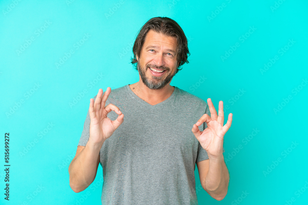 Senior dutch man isolated on blue background showing ok sign with two hands Senior dutch man isolated on blue background showing ok sign with two hands