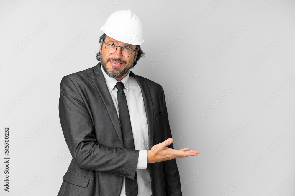 Young architect man with helmet over isolated background presenting an idea while looking smiling towards Young architect man with helmet over isolated background presenting an idea while looking smiling towards