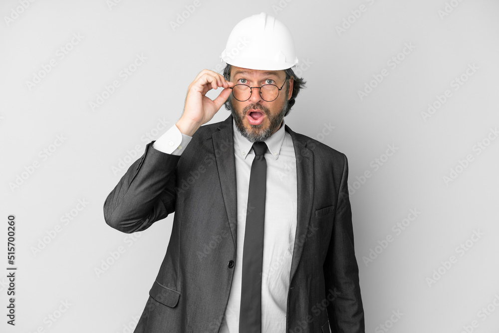 Young architect man with helmet over isolated background with glasses and surprised Young architect man with helmet over isolated background with glasses and surprised