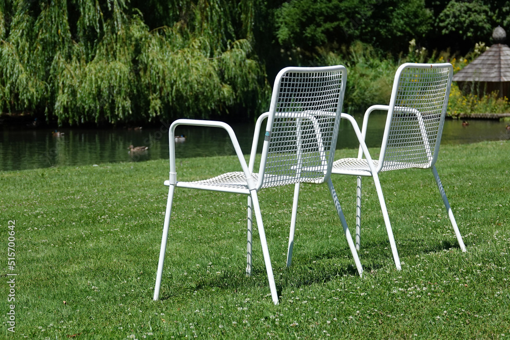 Zwei weisse Metallstühle auf einer grünen Wiese vor einem Ententeich Zwei weisse Metallstühle auf einer grünen Wiese vor einem Ententeich