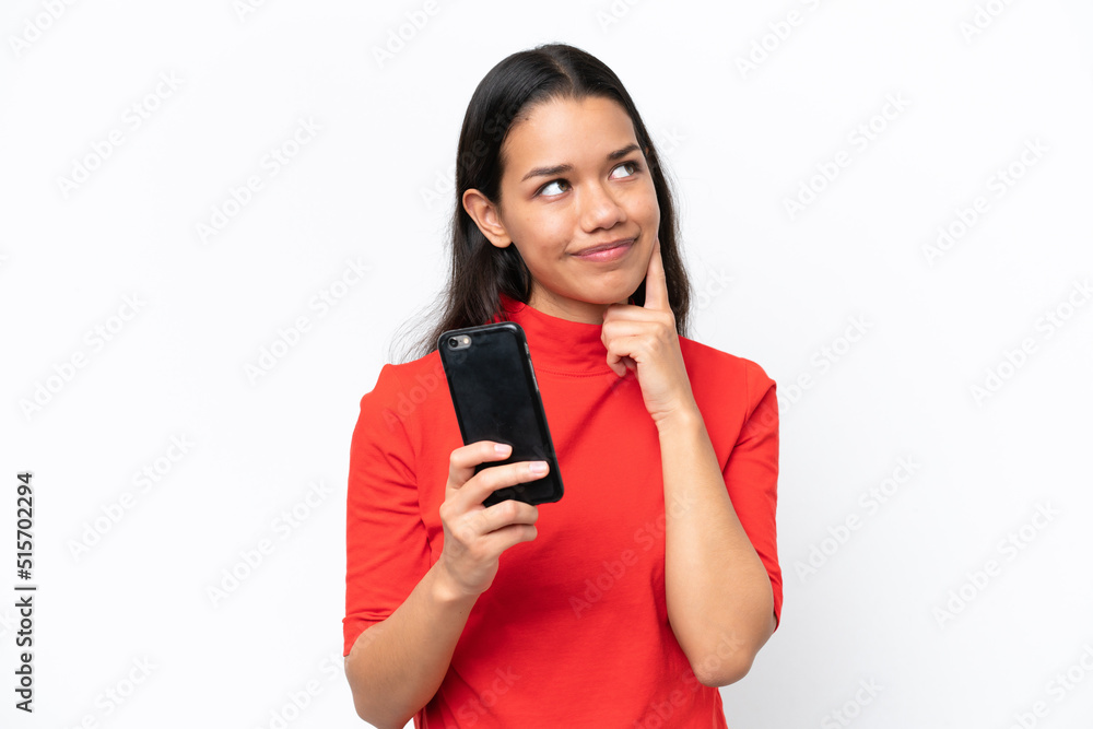 Young Colombian woman isolated on white background using mobile phone and thinking Young Colombian woman isolated on white background using mobile phone and thinking